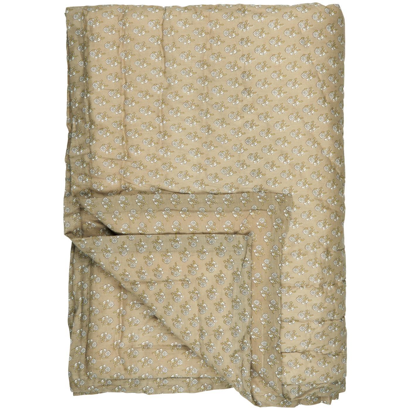 Une grande couverture beige ornée d'un motif floral discret, composée de petites fleurs blanches et vertes, est soigneusement étalée. Un coin de la couverture est replié pour montrer l'épaisseur du tissu et la texture matelassée, ajoutant une touche de confort visuel.
