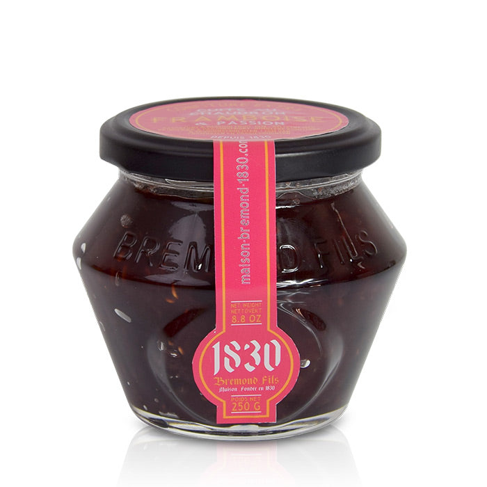 Un pot en verre contenant de la confiture extra de framboise et passion de la marque Maison Brémond. Le couvercle est noir et l'étiquette est rose, indiquant 'Confiture extra framboise & passion' avec un poids net de 250 g et un logo en forme de cercle avec le nom de la marque '1830 Brémond Fils'.