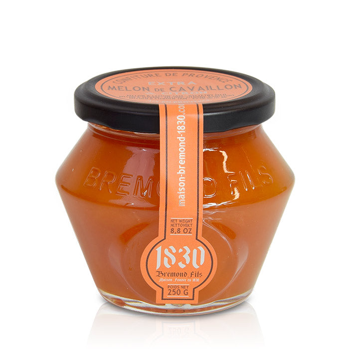 Un pot en verre contenant de la confiture extra de melon de Cavaillon de la marque Maison Brémond. Le couvercle est noir et l'étiquette est orange, indiquant 'Confiture de Provence Extra Melon de Cavaillon' avec un poids net de 250 g et un logo en forme de cercle avec le nom de la marque '1830 Brémond Fils'.